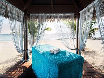 Massagebereich mit türkisfarbener Liege unter Pavillon am Strand mit Blick aufs Meer