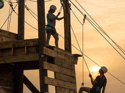 Zwei Personen klettern an einem Seilparcours im Sonnenuntergang.