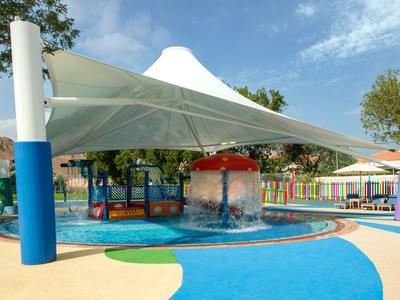 Bunter Wasserspielplatz mit Sonnensegel und Wasserfontäne für Kinder in einem Hotel.