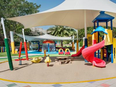 Bunter Kinderspielplatz mit Schaukel, Rutsche und Sonneschutzdach in einem Hotelbereich.