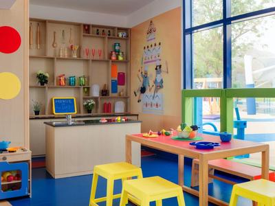 Bunter Kinderspielraum mit Tischen, Stühlen, Regalen und großem Fenster