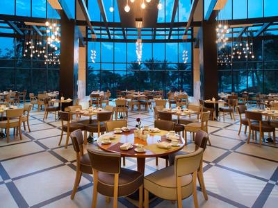 Großer, moderner Speisesaal mit runden Tischen, Holzstühlen und bodentiefen Fenstern bei Dämmerung.