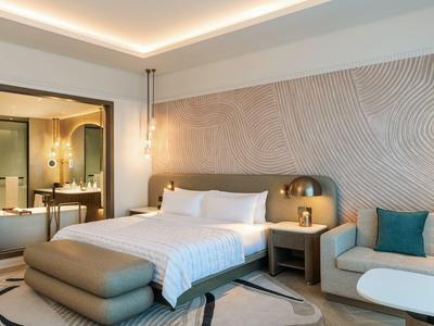 Modernes Hotelzimmer mit großem Bett, Sitzbereich und Blick ins Badezimmer.