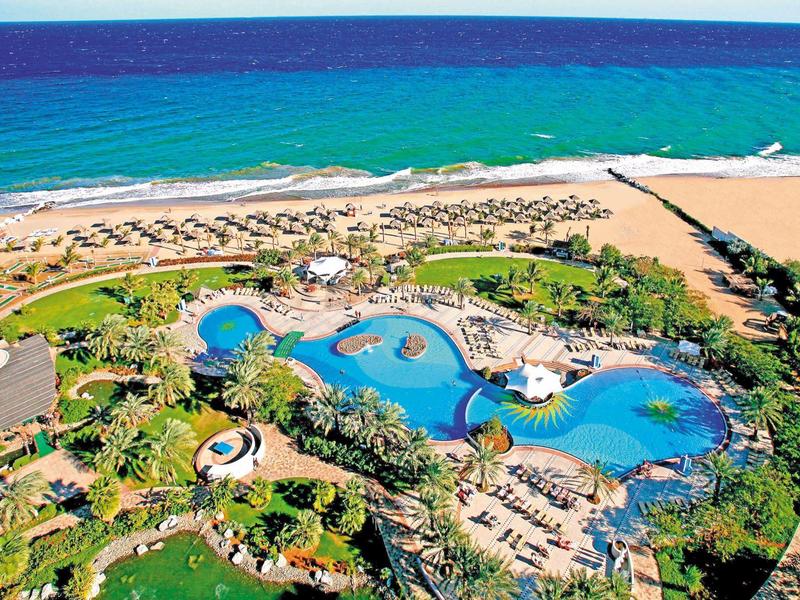 Luftaufnahme eines Resorts mit mehreren Pools am Strand und blauer Meereskulisse.