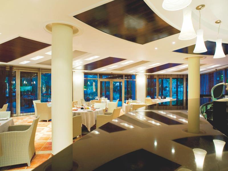 Modernes Hotelrestaurant mit weißen Stühlen, großen Fenstern und warmem Ambiente bei Dämmerung.