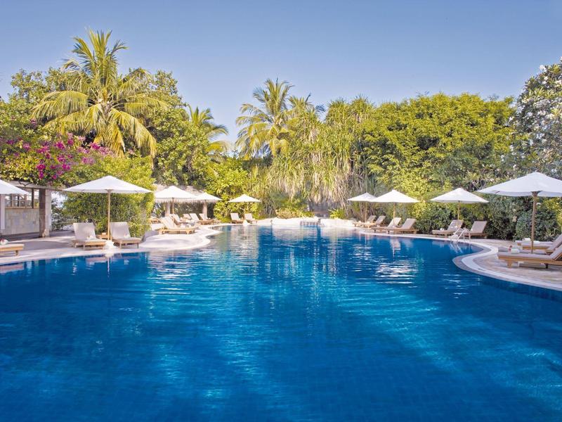 Großer Pool mit Sonnenschirmen und Liegestühlen in tropischer Hotelanlage.