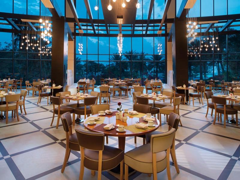 Großer, moderner Speisesaal mit runden Tischen und Panoramafenstern am Abend.