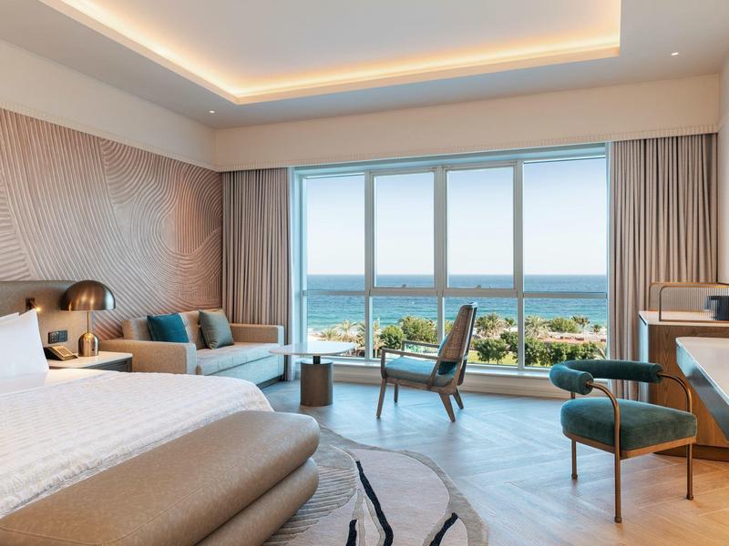 Modernes Hotelzimmer mit Meerblick, bequemen Betten und Sitzbereich vor großen Fenstern.