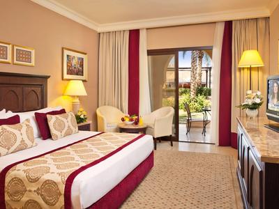 Helles Hotelzimmer mit Doppelbett, Sessel, Balkon und Fernseher.