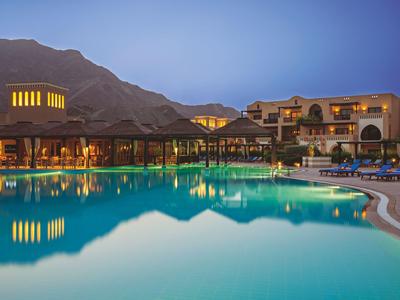 Abendaufnahme eines ruhigen Schwimmbads vor einem Hotel mit Bergen im Hintergrund