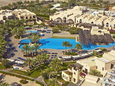 Große Hotelanlage mit mehreren Gebäuden, einem großen Pool mit Insel und umliegenden Palmen.