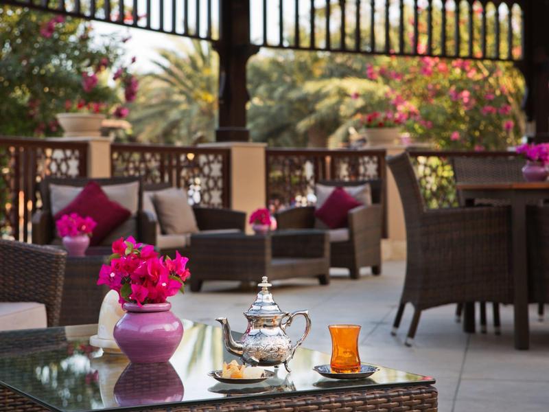 Sitzbereich mit Korbmöbeln und einem Teeservice auf einem Glas-Couchtisch in einem Gartenhotel.