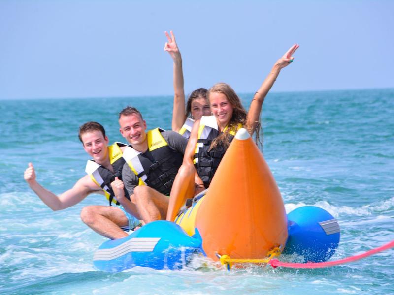 Vier Personen in Schwimmwesten auf einem Bananenboot im Meer bei sonnigem Wetter