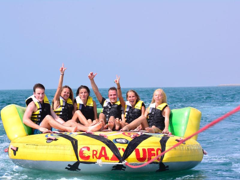 Sechs Personen mit Schwimmwesten sitzen auf einem gelben Bananenboot im Meer.