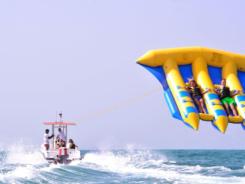 Personen auf einem Boot und Dreier-Wasserschlitten auf dem Meer bei klarem Himmel