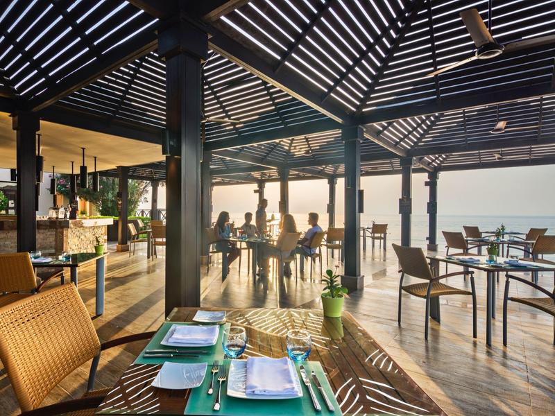 Offener Speisebereich mit Holzmöbeln und Blick auf das Wasser bei Sonnenuntergang.