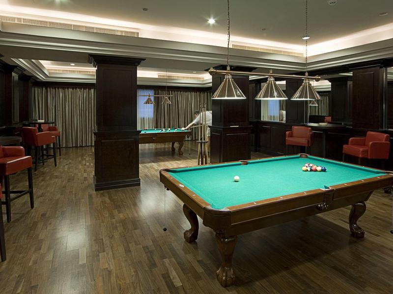 Eleganter Billardraum mit Holzboden, grünen Tischen und moderner Beleuchtung.