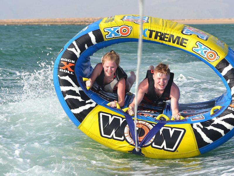 Zwei Menschen liegen auf einem bunten, runden Wassersportreifen auf dem Wasser.