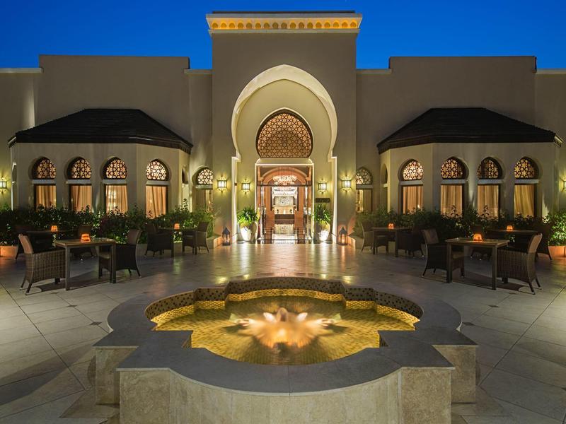 Abendansicht eines beleuchteten Hotels mit einem dekorativen Springbrunnen im Vordergrund.