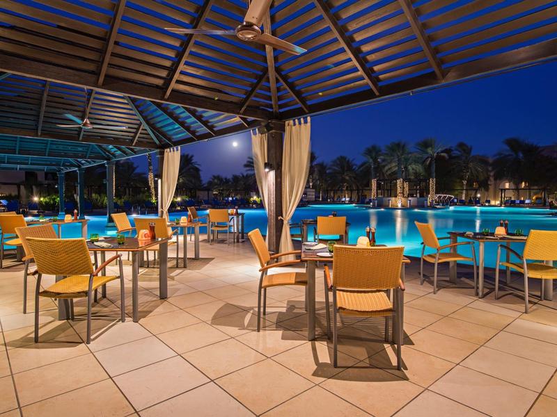 Außenrestaurant mit gelben Stühlen und Blick auf einen beleuchteten Pool bei Nacht