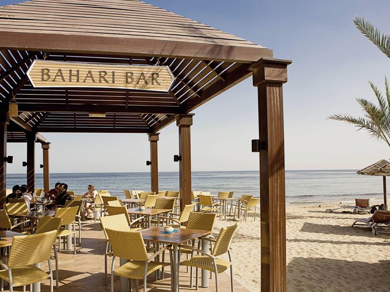 Offener Barbereich mit Tischen und Stühlen am Strand mit Blick aufs Meer.