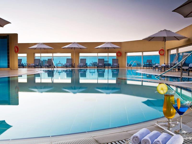 Moderner Außenpool mit Liegestühlen, Sonnenschirmen und Getränken am Rand bei Sonnenuntergang.