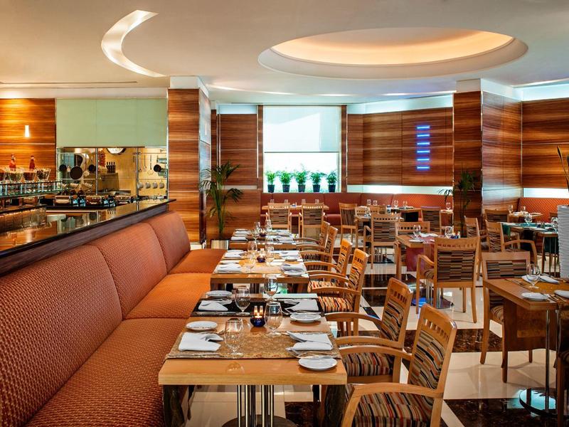 Modernes Restaurant mit Holzmöbeln, orangenen Sitzen, runden Deckenlichtern und großen Fenstern.