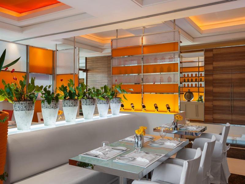 Modernes Restaurant mit weißen Tischen, Stühlen, Pflanzen und warmem orangefarbenem Licht.