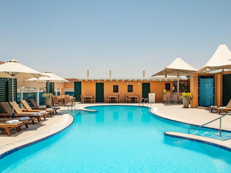 Moderner Hotelpool mit Liegestühlen und Sonnenschirmen unter klarem Himmel