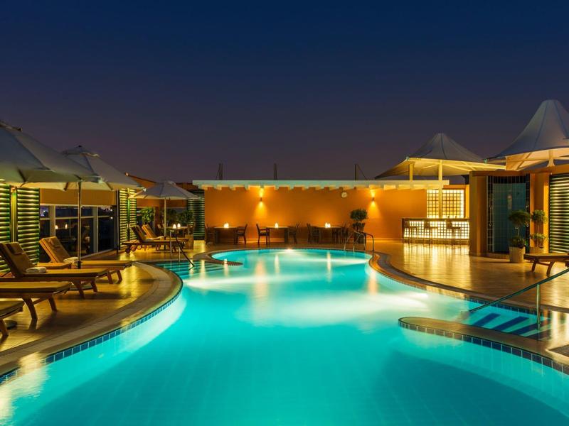 Beleuchteter Außenpool mit Liegestühlen und modernen Sonnenschirmen bei Nacht.