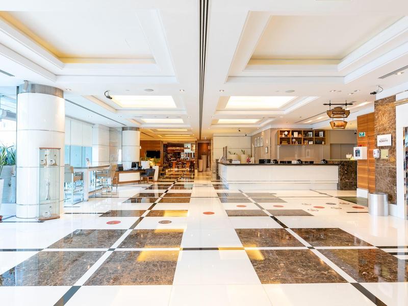 Weitläufige Hotellobby mit glänzendem Marmorfußboden, hellen Wänden und moderner Theke.