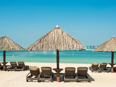 Drei Strohdach-Schirme mit Liegestühlen auf weißem Sandstrand und türkisfarbenem Meer darunter.
