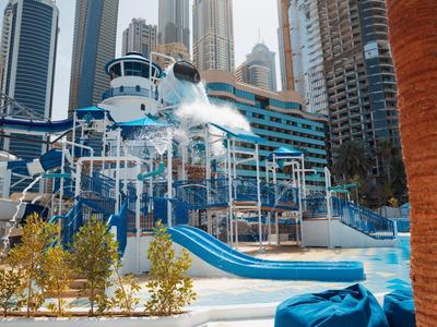 Wasserspielplatz mit Rutschen, blauen und weißen Elementen, umgeben von Hochhäusern und Palmen.