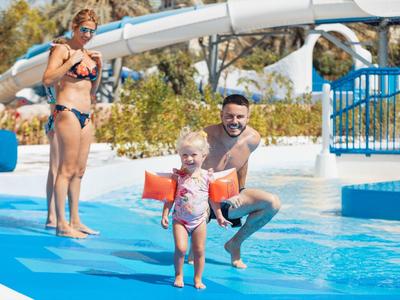 Kinderfreundliche Wasserrutsche mit Eltern, die ein kleines Kind auf blauem Beckenrand begleiten.