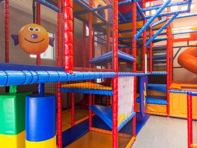 Buntes Indoor-Klettergerüst mit Netzen, Rutschen und weichen Polstern in einem Spielzimmer.