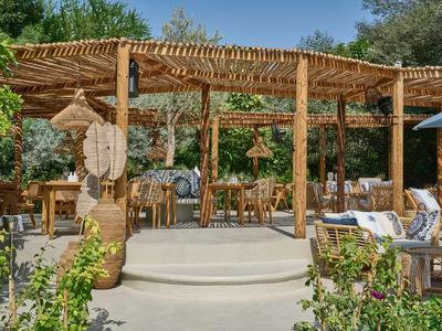 Offener, rustikaler Sitzbereich mit Holzpergola und Gartenpflanzen in einem Hotelgarten.