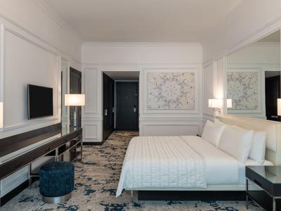 Modernes Hotelzimmer mit großem Bett, Teppichboden, Schreibtisch, Fernseher und sanfter Beleuchtung.