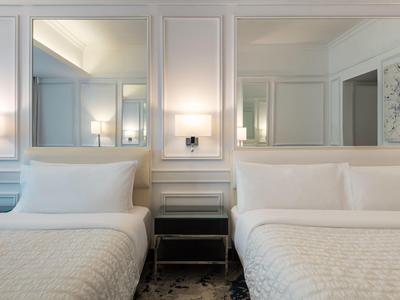 Zwei weiße Betten mit Kissen, schwarzer Nachttisch und zwei große Spiegel an weißer Wand.