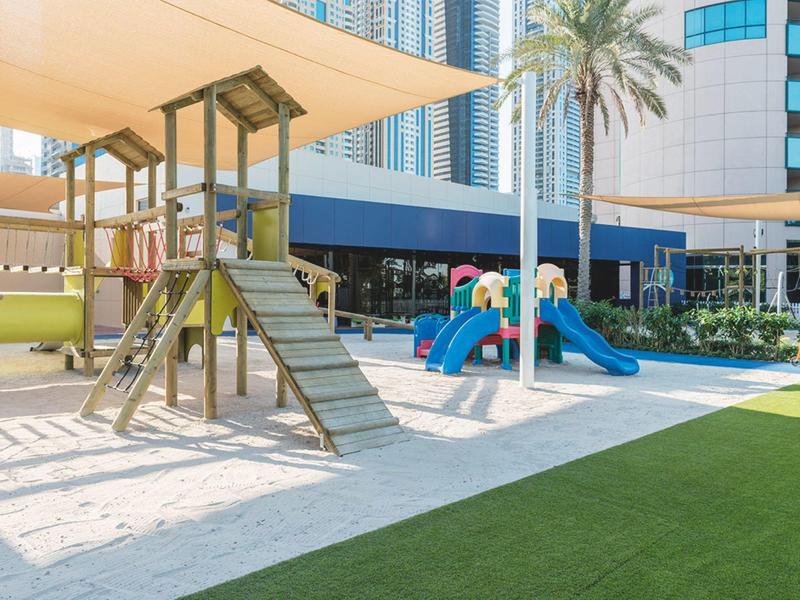 Moderner Spielplatz mit Klettergerüst, Schaukeln, bunten Rutschen und Sonnenschutz in urbaner Umgebung.