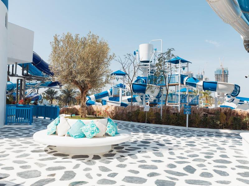 Moderner Außenbereich mit weiß-blauem Farbschema, runder Sitzbank und Wasserpark-Strukturen im Hintergrund.