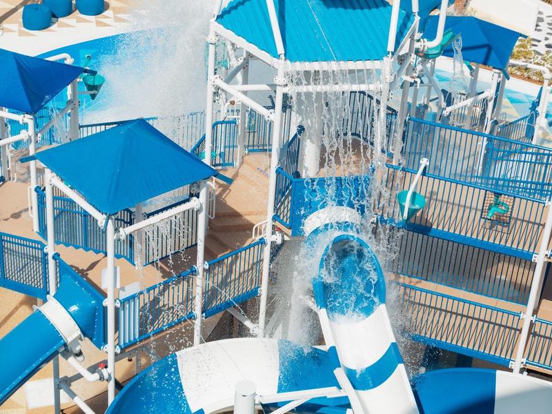 Wasserpark mit blauen und weißen Rutschen, Wasserbecken und erhöhten Plattformen aus Metall.