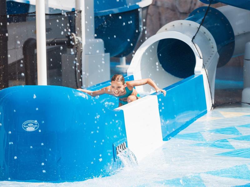 Person rutscht eine blaue Wasserrutsche in ein Schwimmbecken hinunter