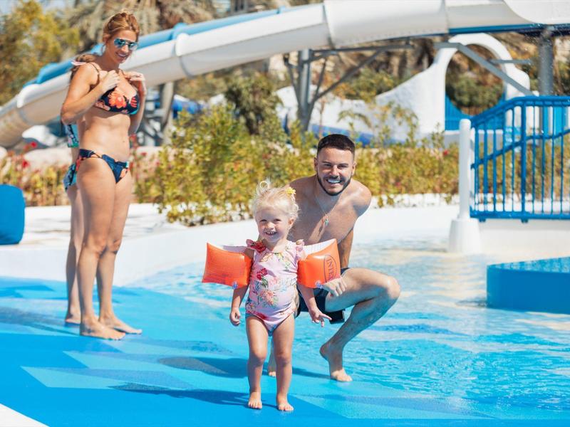 Kinderfreundliche Wasserrutsche mit Eltern, die ein kleines Kind auf blauem Beckenrand begleiten.