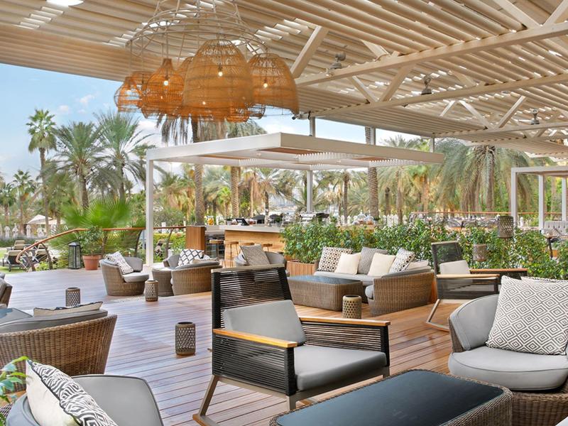 Offener Lounge-Bereich mit Rattanmöbeln, Polstern, Holzboden und dekorativen Lampen unter Dach.