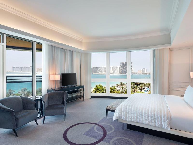 Helles Schlafzimmer mit großem Fenster, Doppelbett, zwei Sesseln und TV, moderner Stil.