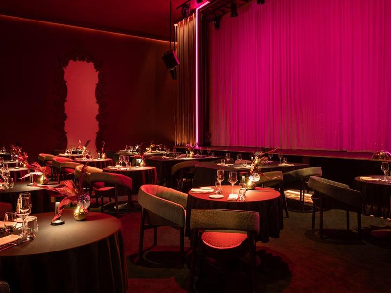 Elegantes Restaurant mit rundem Tischen, roten Stühlen und rotem Lichtambiente.