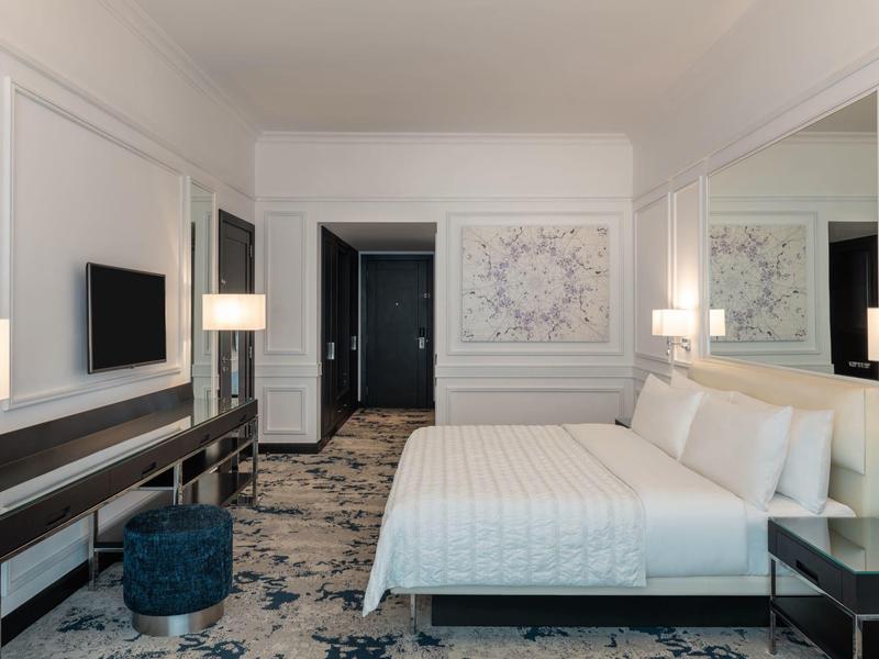 Modernes Hotelzimmer mit großem Bett, Teppichboden, Schreibtisch, Fernseher und sanfter Beleuchtung.