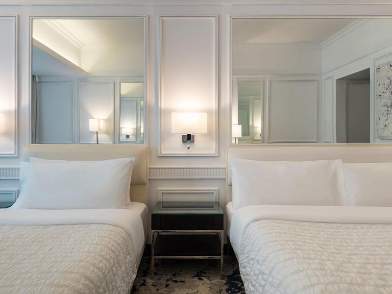 Zwei weiße Betten mit Kissen, schwarzer Nachttisch und zwei große Spiegel an weißer Wand.