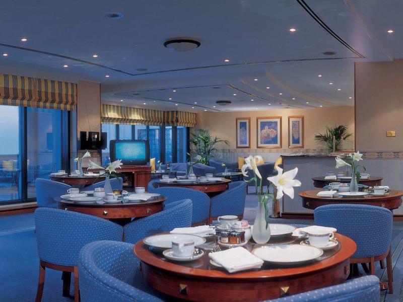 Elegantes, modernes Restaurant mit blauen Teppichen, runden Holztischen und großen Panoramafenstern.