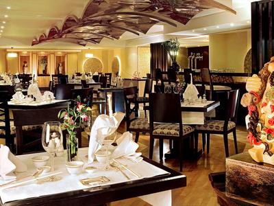 Elegantes Restaurant mit dunklen Holztischen, weiß gedeckten Plätzen und großer Buddha-Statue.